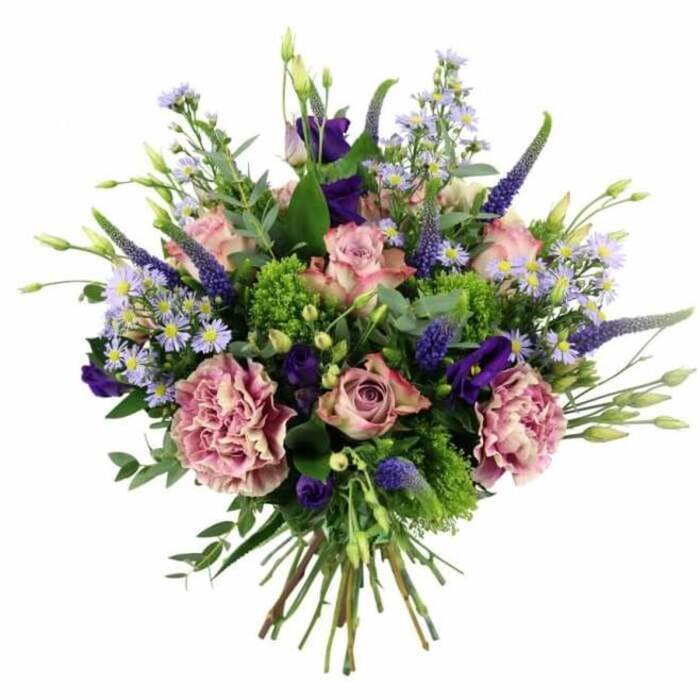 Captured from a slightly overhead angle against a stark white background, this hand-tied bouquet radiates the kind of quiet sophistication you might associate with a design studio off Clerkenwell Green. The flowers form a generous, rounded dome, with soft pink and mauve tones gently blending into deeper purples and vivid greens. At the centre, several pastel pink roses open in graceful spirals, their petals tinted with deeper rose at the heart and fading toward pale blush at the edges. Some blooms are still half closed, holding their shape like elegant sculptures, while others are more relaxed, giving the bouquet a sense of movement and natural ease. Among them, large ruffled carnations in dusty rose and purple-mauve unfold in textured layers, their frilled edges echoing delicate fabric pleats. Shooting upwards in slender arcs, deep lavender-blue Veronica spikes add striking vertical accents, creating a sense of height without overwhelming the softer blossoms. Tucked between these taller forms, bell-shaped lisianthus in rich purple tones and clusters of tiny, aster-like daisies in lavender and periwinkle introduce both depth and a cloud-like lightness. The daisy centres glow with small dots of yellow, lending a cheerful brightness. Surrounding and supporting the blooms is a varied collar of greenery: lime-toned textural filler, perhaps green trick dianthus or sedum, sits alongside cool, silvery eucalyptus and other fresh foliage, offering contrast in both colour and texture. Below the lush flower heads, the stems are visible, gathered neatly and tightly bound, evidence of a skilled hand-tied technique ready to slip into a vase on a Clerkenwell kitchen table or office desk. The bouquet conveys a sense of modern romance and refined celebration, perfectly suited to birthdays, anniversaries, or thoughtful deliveries to homes and studios around Farringdon and St John Street.