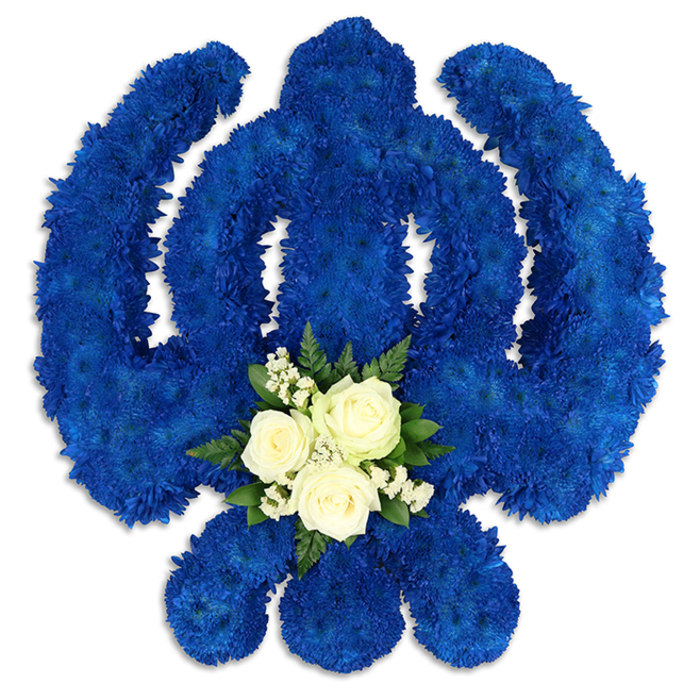 An elaborate Sikh Khanda floral tribute dominates the image, carefully positioned against a bright white background so that every detail of the design is clearly visible. The iconic shape - central double-edged sword, circular chakkar, and two outward-curving kirpans - has been expertly sculpted from a dense carpet of royal blue chrysanthemum blooms. Each small floret is placed tightly against the next, forming a velvety, uniform surface that feels almost like rich fabric or ceremonial cloth. The deep, dignified blue colour conveys strength, loyalty, and spiritual depth, evoking the calm, reflective moments you might experience walking through the quieter corners of Clerkenwell early in the morning. Light falls softly across the petals, creating gentle highlights and shadows that add dimension to the emblem and make the raised contours of the symbol appear almost three-dimensional. At the lower centre of the Khanda, where the stem of the sword meets the circular form, a contrasting floral accent gently softens the bold geometry. Three creamy white roses, their petals layered and slightly open, nestle together within a halo of tiny white filler flowers and sprigs of fresh green foliage. The white and green cluster offers a serene counterpoint to the intense blue chrysanthemums, suggesting peace, remembrance, and a message of pure, loving farewell. This floral Khanda would feel at home at a Sikh funeral, memorial, or celebration of life service around Clerkenwell, placed near the altar or beside a casket as a proud expression of faith and heritage. It appears to be the work of an experienced local florist, sensitive to tradition and attentive to every symbolic detail.