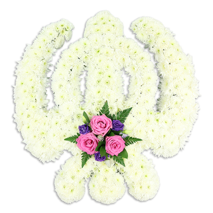 A reverent Sikh Khanda tribute dominates the composition, its sacred silhouette crafted entirely from densely clustered white chrysanthemums that create a pristine, uniform surface. The double-edged central sword stands tall and straight, its edges subtly defined by the careful placement of blooms, while the circular chakra wraps around it with flawless symmetry. On either side, the two downward-curving kirpans stretch out like protective arms, their shapes so precise that the emblem appears almost drawn in flowers. The texture is rich but controlled, each floret pressed closely to its neighbour, producing a soft, cushion-like finish that evokes purity, serenity, and quiet strength. Anchoring the design at the bottom, nestled where the kirpans nearly touch, is a compact cluster of accent flowers: three prominent pink roses, their petals curled in concentric layers, are paired with smaller deep purple blossoms and threaded through with feathery green fern leaves. This pocket of colour offers a gentle contrast to the otherwise all-white tribute, suggesting the warmth of family love within the larger frame of spiritual faith. The arrangement is shown against a clear white background, with subtle shadows beneath giving it depth and the sense of being ready to be carried into a service. This is the kind of bespoke piece a family in Clerkenwell or nearby Barbican might choose for a Sikh funeral or memorial, placing it at the front of the Gurdwara to honour a loved one's beliefs. Its calm presence, born of careful craftsmanship and local floristry expertise, conveys dignity, remembrance, and enduring connection.