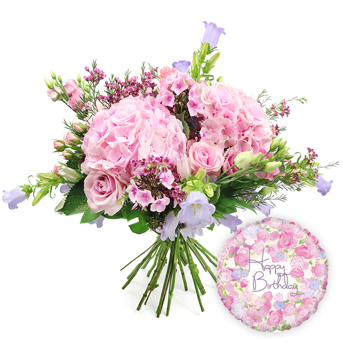 Set against a crisp white background, this hand-tied birthday bouquet looks as if it has just been arranged on a light-filled workbench in Clerkenwell, its pastel colours and rounded shape conveying warmth and celebration. The central focus is a cluster of generous pink hydrangea heads, their countless tiny petals overlapping to form soft, voluminous domes that suggest comfort and abundance. Tucked sensitively among them are soft pink roses in varying stages of bloom: some fully open with their classic spiral of petals on display, others still partially closed so that only a hint of their swirling centres is visible. Interspersed throughout, dainty fuchsia-pink filler flowers-akin to waxflower-provide flickers of deeper colour and a fine, feathery texture that contrasts with the bolder, more substantial blooms. Rising a little above the dome of hydrangeas and roses, delicate campanula stems carry upward-facing, bell-shaped flowers in lavender and periwinkle shades, their cool tones adding grace and a touch of whimsical movement. The bouquet is framed by an abundance of fresh greenery: broad, supportive leaves at the base and more slender, elongated foliage around the edges, giving the arrangement an organic, garden-sourced feel that would suit a stroll along Clerkenwell Road or through nearby parks. The stems are left visible where they are carefully bound at the bottom, underlining the hand-tied craftsmanship behind the design. To the lower right, a round metallic birthday balloon gleams softly, decorated with a detailed all-over floral pattern of small roses and buds in pink, cream, and lilac hues. Across its centre, in decorative purple script, the words Happy Birthday are clearly written, completing the celebratory pairing. Together, bouquet and balloon form a charming visual for birthday flowers in Clerkenwell, ideal for marking special days in flats near Exmouth Market or offices close to Farringdon Station.