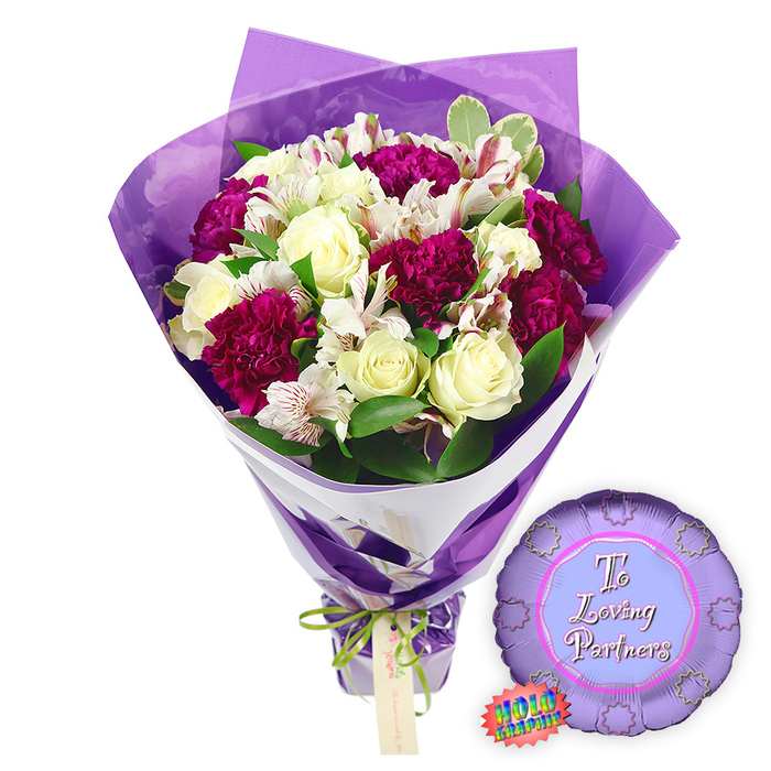 In this image, a thoughtfully arranged romantic bouquet is paired with a metallic balloon, both resting against a bright white background that highlights every detail of the design. At the centre of the hand-tied flowers are several creamy white roses, their petals spiralling tightly in that classic rose shape that speaks of timeless love and freshly cut elegance. Nestled among them are numerous deep magenta to burgundy carnations, each bloom formed from finely ruffled petals that layer into rich, cushion-like clusters, creating a sense of warmth and intensity. White alstroemeria blooms, also known as Peruvian lilies, are scattered throughout the bouquet, their slender petals marked with fine reddish-brown streaks and tiny speckles on the inner surfaces, giving the whole arrangement an intricate, almost illustrated quality. Around the flowers, lush greenery fans out, with glossy green leaves and touches of variegated foliage edged in soft cream, building a full, rounded silhouette that would look as at home in a Clerkenwell loft overlooking Exmouth Market as on a cosy dining table near Rosebery Avenue. The florist has wrapped the bouquet in an inner layer of crisp white paper that appears as a clean diagonal band, and an outer layer of translucent, crinkled purple cellophane that softens the edges and glows gently against the petals. The stems are gathered tightly at the base and tied with a slim, bright green satin ribbon, finished in a small bow, from which a light brown rectangular gift tag dangles, ready to bear a personal love note. To the right of the bouquet, resting on the same white surface, sits a round purple foil balloon with a scalloped, rosette-like edge and a paler purple centre printed with the words To Loving Partners in graceful pink script. A tiny rainbow holographic sticker clings to one side of the balloon, catching the light and adding a fun, celebratory flare. This image encapsulates a tender, elegant expression of partnership, ideal for anniversaries, romantic milestones, or thoughtful same-day flower deliveries across Clerkenwell and nearby Farringdon.