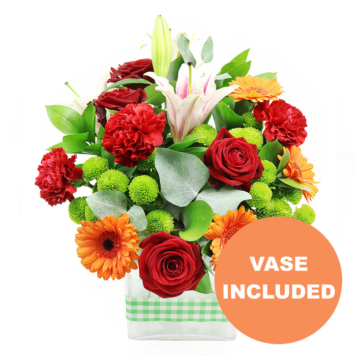 A richly coloured mixed flower arrangement is captured in crisp detail, displayed in a sleek, rectangular glass vase banded with a light green and white gingham ribbon that gives the design a relaxed, homely feel suited to Clerkenwell townhouses and warehouse conversions. At the core of the bouquet, several deep crimson red roses stand out, their velvety petals tightly layered to form classic spirals of colour. Around them, red-orange carnations with gently ruffled edges add volume and texture, their frillier petals creating a soft contrast against the smoothness of the roses. Bright orange gerbera daisies with dark, almost black centres are dotted through the display, their wide, flat petals radiating like little sunbursts and bringing a lively shot of warmth to the composition. Clusters of fresh lime-green pompom chrysanthemums are tucked between the larger blooms, each rounded head made up of tiny, packed petals that give the whole arrangement a contemporary, playful twist. Rising above and through the bouquet, white Oriental lilies with blush-pink striping open into broad, star-shaped trumpets; some are fully open, showing delicate stamens dusted with pollen, while others remain as sleek green-tipped buds that hint at flowers still to come. Deep green foliage and sprigs of silvery eucalyptus weave around the stems, adding depth, fragrance, and a soft, misty contrast to the brighter tones. The composition sits against a stark white background, making the reds, oranges, greens, and whites feel especially vivid, as though freshly arranged in a Clerkenwell Flowers studio just off St John's Square. In the bottom right corner, a circular orange overlay with bold white capital lettering reads VASE INCLUDED, overlapping the vase slightly to emphasise that this sturdy glass container forms part of the complete, ready-to-display gift.