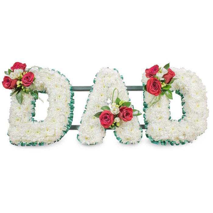 A poignant and meticulously formed funeral display spelling DAD in three large capital letters, each letter entirely covered with hundreds of tiny, pristine white chrysanthemums to create a continuous, velvety texture that reads calm and reverent from every angle. The perimeter of each letter is neatly trimmed with a deep emerald green pleated ribbon, lending sharp definition against the white blooms and reinforcing the architectural form. Strategic clusters of deep red garden roses punctuate the composition-one perched on the upper left curve of the first D, a matching grouping nestled in the A, and a final spray on the upper right curve of the second D-each accented with small white freesia or lisianthus buds and a generous sweep of glossy green foliage. Thin loops of bear grass add a fine sculptural line that lifts the clusters and introduces a subtle movement across the static letterforms. Slightly visible behind the flowers are dark green or black metal bars that provide structural cohesion and discreet stability for transporting and setting the tribute at a funeral venue. Bathed in soft, diffuse light against a bright white background, the contrast between serene whites and intense ruby reds becomes quietly expressive: chrysanthemum for purity and devoted love, rose for deep respect. A Clerkenwell-area florist might prepare this arrangement for services at local churches near Clerkenwell Green or for placement at a graveside after a service in St John's Square; the piece reads as both a heartfelt personal message and a carefully engineered floral composition.