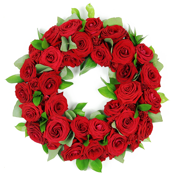 Deeply symbolic and visually striking, this circular wreath is meticulously crafted from dozens of vibrant, deep red roses. The white background makes the blooms glow, their petals opening from tight buds to full, velvety fans of crimson. Interwoven among the blossoms, clusters of fresh, glossy green foliage-eucalyptus-like broad leaves and slender ruscus-create a lush tapestry that enhances depth and texture. The wreath reads as a continuous ring, a timeless tribute inviting quiet reflection. It speaks of love, remembrance, and respect, and its fullness suggests generous care and generous memory. In Clerkenwell, we often place it near St. John's Gate or by the churchyard, with the same-day delivery option to nearby streets such as Clerkenwell Road, Farringdon, and the City. Crafted by Clerkenwell Flowers, it arrives vibrant and fragrant, ready to be laid with dignity at the service.