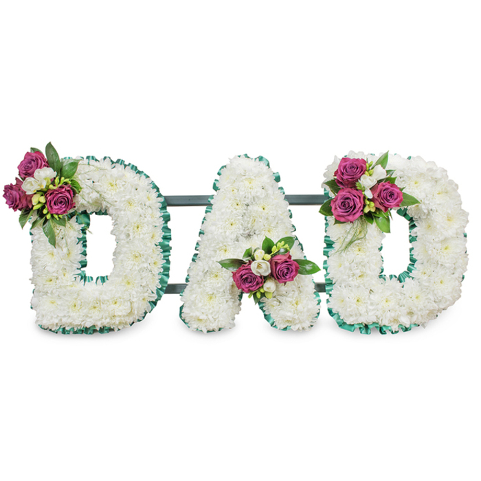A solemn yet tender memorial arrangement spells DAD in large, capital letters made entirely from compact, snowy white chrysanthemum heads, their soft, ruffled petals forming a continuous, cloud-like surface that reads both pure and substantial. The letters are outlined by a vivid emerald-green pleated ribbon which follows the outer and inner edges with precise, ruffled detail, brightening the white while preserving a respectful formality. Small, carefully arranged spray clusters of vibrant magenta roses punctuate each letter: the first D bears a bloom cluster at its upper left curve, the A holds a cluster settled into its lower central V, and the final D mirrors the first with a matching grouping on the upper right. Each rose cluster is framed by tiny white freesia or similar spray blooms and rich dark-green foliage, lending contrast in texture, subtle perfume and a deep, garden-like depth. A discreet, dark green horizontal bar runs behind the letters, suggesting a stable, self-supporting display for viewing at a chapel, wake or graveside service. The clean white backdrop and soft directional light make the white chrysanthemum surfaces appear almost luminous, while the magenta accents read as personal, affectionate markers of memory. Crafted by Clerkenwell Flowers for families across Clerkenwell, Farringdon and nearby Smithfield, this tribute carries the quiet language of love and remembrance-an artisan floral letterpiece designed to honour a father with dignity and warmth.