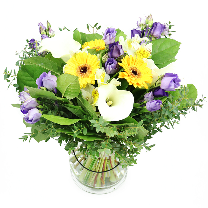 From above, the mixed bouquet unfurls like a painter's palette, the clear glass vase acting as a prism for colour and light. The dominant yellow Gerbera daisies with their bold centers catch the eye first, their cheerful faces set against the ivory glow of Calla lilies, and the lavender Lisianthus that creep in with their soft, ruffled edges. Smaller white Alstroemeria with hints of yellow break the plane and add delicate texture. The greenery is lush and varied: slender stems of eucalyptus that glint with a silvery sheen, broad green leaves that anchor the arrangement, and wispy filler greens that lend air and depth. The stems run neatly through the water, visible through the transparent vase, and a slim black ribbon inside the vase holds the stems in a tidy, natural arrangement. The overall effect is one of balance between brightness and refinement, a contemporary Clerkenwell piece ready to grace a windowsill near Hatton Garden or a desk on Farringdon Road. Clerkenwell Flowers designs for real homes and offices, with same-day delivery available across Clerkenwell, Islington, and surrounding districts, ensuring freshness that lasts and a sense of place in every petal. This arrangement speaks of celebrations, quiet gratitude, and the everyday elegance that defines this part of London.