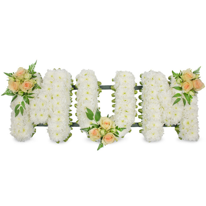A graceful floral memorial spells out MUM in three large, upright letters, composed entirely of small, snow-white spray chrysanthemums. Every letter is densely filled so the blooms create a plush, almost quilted texture, with each tiny petal contributing to a sense of softness and purity. The design is photographed against a stark white background, which exaggerates the clean lines and generous proportions of the tribute, while hints of dark green frame or ribbon peek around the edges, subtly defining the shapes without distracting from the mass of flowers. Delicately warming the cool expanse of white, three clusters of roses in gentle peach and blush tones are positioned with deliberate care. One cluster, a mix of fully opened roses and rounded buds, nestles on the upper left arm of the first M. Another sits securely at the base of the U, softening the inner curve of the letter. The last cluster mirrors the first, poised on the upper right arm of the final M, completing a balanced and harmonious composition. Around the roses, sprigs of fresh greenery-light, feathery ferns and richer, glossy leaves-add movement and a subtle woodland feel. The overall mood is serene and reverent, conveying love, gratitude, and remembrance for a mother's steady presence. This style of floral lettering, similar to those crafted by Clerkenwell Flowers for services near Hatton Garden or around Clerkenwell Green, would typically rest beside the coffin or at the front of a chapel during a funeral or celebration of life, offering a heartfelt, personalised tribute that speaks quietly but powerfully of family bonds and enduring affection.