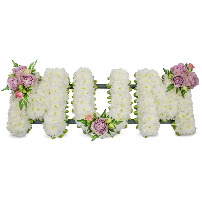 A generous, heartfelt floral tribute spells out the word 'MUM' in bold capital letters, each letter densely covered in tiny, crisp white spray chrysanthemums that together form a soft, cloud-like surface. The pristine white conveys solemnity and remembrance, while three small clusters of pastel colour are positioned to bring warmth and tenderness: a combination of lavender roses and a pale pink rosebud crowns the upper left arm of the first 'M', another similar cluster nestles into the gentle curve of the 'U', and a matching grouping graces the upper right arm of the final 'M'. Between these accents, vibrant green foliage, including delicate fern fronds and lighter green leaves, weaves through the blooms to provide texture, depth and a fresh contrast to the white. A subtle dark green frame-likely ribbon-wrapped or moss-covered floral foam-traces the letters' bases and keeps the tribute upright and unified for standing display at a funeral, chapel service or graveside. The overall effect is one of quiet dignity: the cool, powdery scent of chrysanthemums beneath the soft, sweet perfume of roses, a composition that reads as both personal and timeless. As Clerkenwell Flowers, serving clients across Clerkenwell, Exmouth Market and Farringdon, we place these tributes with care so they sit with balance and clarity in small local chapels or crematorium viewing rooms, offering comfort through beauty and thoughtful craftsmanship.