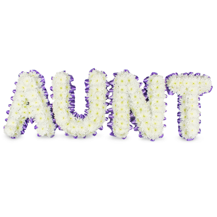 A handcrafted memorial spells out AUNT in large, elegant capitals, each letter densely faced with immaculate white spray chrysanthemums whose compact petals create a cloudlike, tactile surface. Here the tiniest details matter: some florets reveal pale yellow centres that read as soft points of warmth amid the sea of white, while the chrysanthemum petals are ever so slightly ruffled, catching the light and producing a subtle, comforting texture. The perimeter of every letter is outlined with deep purple satin ribbon, carefully ruffled and pleated so its sheen whispers across the composition and provides a refined, contrasting edge. The ribbon's folds and the flowers' layered petals together add depth and dimension; faint grey shadows beneath the frames punctuate how the letters lift off the white backdrop into real space. There is an understated fragrance-clean, green and slightly dewy-that seems to belong to early morning chapel arrangements, the kind that settles gently in a room of friends and family. As a florist who has worked for services around Clerkenwell Green, Spa Fields and the markets of Exmouth Market, I choose this palette because it balances respect with affection: white for remembrance, purple for dignity, and a handcrafted form to say a personal goodbye. The composition is meant to be read at the front of a service, to sit quietly on an easel or stand and convey both reverence and the warmth of a cherished familial bond, crafted with steadiness and care for delivery within the local area.