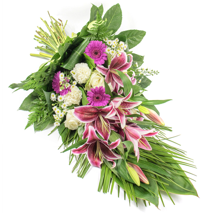 Set against a clean white backdrop, this elegant funeral spray stretches diagonally from the upper left corner to the lower right, creating a flowing crescent shape that suggests a gentle final journey. A cluster of bold Stargazer lilies forms the focal point: each bloom features rich fuchsia-pink petals, edged in crisp white and dusted with dark burgundy speckles, while several elongated buds, tinged green and pink, promise blossoms yet to open. Around these lilies, vibrant magenta gerbera daisies lend a contemporary brightness, their flat, daisy-like faces filled with colour and affection. White roses, some tightly closed and others just beginning to open, sit alongside ruffled white carnations, adding layers of softness and traditional grace. Tiny white daisy-like fillers are scattered throughout the design, catching the eye and lending a sense of delicacy and airiness. The surrounding foliage is abundant and textural: broad, glossy dark green leaves form a strong framework; feathery ferns add a light, lacy edge; and long, narrow leaves sweep outward and downward, enhancing the elongated, teardrop silhouette. The stems, neatly bound at the top left, reveal the hand-tied craftsmanship of a local florist used to preparing tributes for Clerkenwell's chapels and memorial spaces. This arrangement feels composed and peaceful, suitable for resting beside a coffin or placing near a photograph at a remembrance gathering. Its blend of vivid pinks, serene whites, and rich greens mirrors the balance between sorrow and gratitude that often accompanies farewells in the Clerkenwell community.