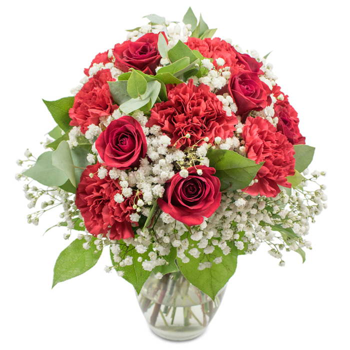 A richly detailed bouquet of red and white flowers is presented in a clear glass vase, isolated against a pristine white backdrop that highlights every colour and texture. The design revolves around several deep crimson roses, their petals tightly wound in perfect spirals, each flower looking poised to unfurl into full bloom. These classic roses are surrounded by plentiful red carnations, whose densely ruffled petals create an almost feathery surface, giving the arrangement a lush and tactile quality. Interspersed among the red blooms is a generous scattering of white baby's breath, the tiny blossoms clustered on fine stems like little puffs of cloud, gently lightening the palette and adding an impression of softness and purity. Nestled between the flowers, fresh greenery offers contrast: the darker, glossy rose leaves sit alongside softer, rounded eucalyptus with its subtle silvery-green tone, bringing depth and a relaxed, contemporary feel that would be perfectly at home in a Clerkenwell studio overlooking the streets near Clerkenwell Green. The bouquet has been shaped into a full, rounded dome, carefully balanced so that the reds, whites, and greens appear in harmonious proportions whichever angle you imagine viewing it from. The clear glass vase has a modest, slightly flared rim and a sturdy base, its transparency revealing the neatly cut stems and clear water, a sign of meticulous floristry. The bright, even lighting makes the reds appear especially vivid and the whites clean and crisp, capturing the sense of a fresh bouquet ready for same-day delivery across Clerkenwell and nearby Farringdon. The overall mood is one of romance and celebration, ideal for anniversaries, Valentine's Day, or any heartfelt gesture that calls for a timeless red-and-white display.