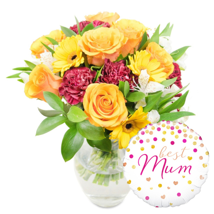 Framed by a stark white background, this celebratory floral arrangement pairs garden-fresh blooms with a sentimental balloon to create a coherent, heartwarming gift. The bouquet is dominated by several plush orange roses - some leaning peach, others a more saturated tangerine - each bloom built from tightly layered petals that open into soft, rounded faces. Interspersed are bright yellow gerbera daisies whose flat, radiating petals surround deep, nearly black centres, providing crisp contrast and a cheerful focal point. Ruffled deep red-to-burgundy carnations supply volume and a rich, velveteen texture that grounds the lighter florals, while small clusters of white alstroemeria with their narrow, slightly freckled petals bring a refined, almost linen-like softness across the arrangement. A variety of green foliage - glossy, broad leaves and slender airy sprigs - creates a lush framework and is visible through the clear glass vase, where carefully cut stems rest in pristine water. To the lower right the round white foil balloon reads best Mum in an elegant fuchsia script, its surface playfully dotted with scattered gold and hot-pink confetti and tiny heart motifs; it overlaps the base of the vase and some lower stems, integrating the balloon with the bouquet rather than leaving it separate. The lighting is even and clean, suggesting studio clarity or a bright morning in Clerkenwell near St John's Square; the overall impression is one of thoughtful craftsmanship and joyful affection, suited to Mother's Day, milestone birthdays or a simple, sincere thank-you.