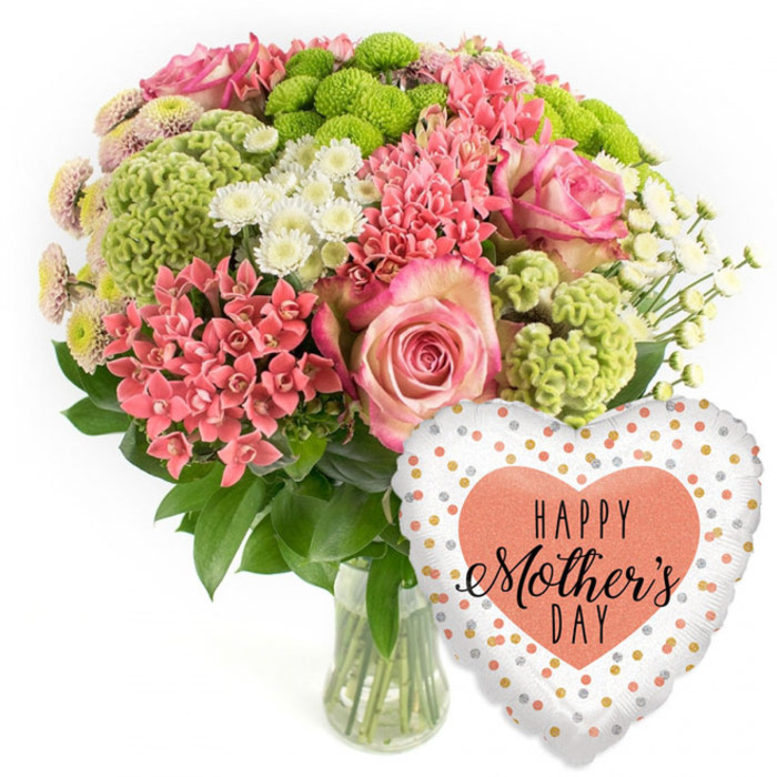 In this softly lit studio-style image, a generous Mother's Day bouquet sits proudly in a clear glass vase, with a celebratory heart-shaped balloon resting to its right, all shown against a spotless white background. The flowers form a lush dome, the kind of balanced, full arrangement you might see prepared in a Clerkenwell workshop for delivery to nearby offices and apartments. Large pink roses immediately draw attention, their layered petals transitioning from deeper, rosy centres to paler, almost white tips, giving a romantic, painterly effect. Nestled around these focal blooms are clusters of coral-pink florets that resemble kalanchoe or spiky spray carnations, each compact head adding a sense of richness and movement. Lime-green button chrysanthemums and velvety, frilled green cockscomb-like blooms punctuate the bouquet with a vivid, contemporary jolt of colour, their rounded and textured forms lending a tactile, moss-like quality. Interwoven among the brighter tones are small white daisy-style chrysanthemums and tiny pastel-tipped blooms, which lighten the arrangement and create a feeling of soft airiness, like early spring light over Clerkenwell Green. Dark, glossy foliage peeks out from beneath and between the flowers, creating contrast and a natural frame that holds the composition together. The clear vase reveals a tangle of stems and clear water, emphasising freshness and professional care. To the lower right, a shiny foil balloon in a heart shape adds an unmistakably festive accent. Its white surface is sprinkled with irregular metallic gold, silver, and peach polka dots, framing a central peach heart emblazoned with the message HAPPY Mother's DAY in black script and bold type. Together, blooms and balloon evoke appreciation, celebration, and the simple joy of sending a thoughtful Mother's Day surprise within the Clerkenwell area.