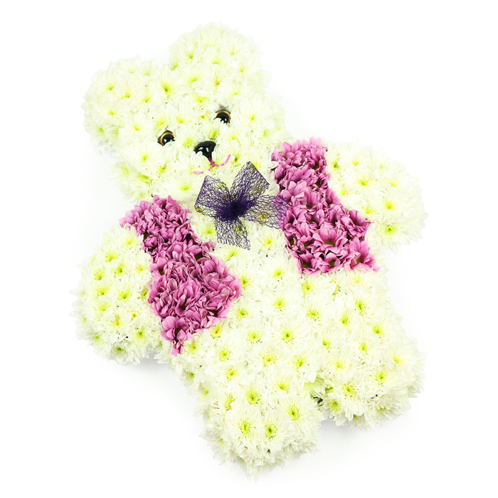 A softly lit floral teddy bear stands out crisply against a pure white backdrop, its design reflecting the thoughtful, detailed work of a Clerkenwell florist familiar with intimate family tributes. The bear's entire form-from rounded ears and domed head to plump belly and short legs-is densely covered with creamy white chrysanthemums. Each bloom is nestled tightly against the next, creating a continuous, velvety surface that looks as gentle as a child's cuddly toy. Hints of buttery cream and pale yellow at the flower centers add depth and warmth, while the feathery petals lend a sense of gentle movement, as if a breeze might ruffle them. The teddy's face is defined with small, dark, button-like eyes and a neat triangle of black at the nose, giving an expression that feels both innocent and quietly protective. A faint, curved line beneath the nose suggests a soft smile, subtle yet full of affection. Across the chest, two rich panels of magenta and rose-pink blooms create a distinctive waistcoat, the colours deep and saturated like summer blossoms in a courtyard off St John Street. These darker petals are slightly more textured and ruffled, offering a cheerful contrast to the pale, plush body. At the neckline sits a delicate bow of sheer violet netting, its translucent loops adding a light, airy touch of refinement. The white background and even lighting make every petal and contour clearly visible, giving the tribute a serene, almost angelic quality. Ideal for funerals, children's memorials, or tender commemorations around Clerkenwell, this floral teddy bear conveys love, protection, and a heartfelt farewell.