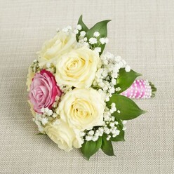 Imagine entering a sunlit Clerkenwell studio, where the scent of fresh-cut roses mingles with artisan energy. Here, a small yet masterfully arranged bouquet awaits, resting gracefully on a pale linen cloth reminiscent of the area's refined style. At its centre, creamy roses-each bloom full and velvety-unfurl their petals in soft spirals. Their serenity is gently interrupted by a single rose in vibrant pink-magenta, a daring dash of colour reflecting the thriving creativity found in nearby Farringdon workshops. Sprigs of feathery baby's breath float among the roses, creating an airy veil that captures the lightness of a spring morning in Spa Fields. Strong emerald greenery frames the bouquet's base, grounding the delicate composition with a touch of lush vitality. The stems are neatly bound in glossy pink satin ribbon, spun through with a spiral of small, gleaming pearls-a modern, distinctly local touch. Every detail reveals the hand of an expert florist committed to making moments memorable, whether for a Clerkenwell loft wedding or a joyful gathering on St John Street. The careful combination of colour, texture, and fragrance creates a bouquet that whispers of romance and creative tradition, making it an exquisite choice for any celebration that values both elegance and a sense of place.