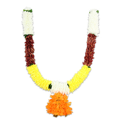 A traditional Indian toran, photographed on a stark white backdrop, presents a carefully considered rhythm of colour and texture that a local Clerkenwell florist would recognise at a glance. Beginning at the top of each arm, dense creamy-white clusters - small, chrysanthemum-like florets - form tidy hanging tabs, their soft, feathery surfaces suggesting a gentle, almost fleece-like touch. Below these ivory sections, the garland shifts into a rich, reddish-brown band: layered, flattened petals and compact bud shapes that add weight and an earthy counterpoint to the lighter top. The curve then unfurls into the main body of the garland, a broad sweep of vivid yellow elements that mimic marigolds, tightly threaded and plush, their ruffled surfaces catching studio light and throwing a cheerful glow across the composition. Intermittent green accents provide crisp separations between hues, like small leaves or woven ribbon. At the centre-bottom, a generous pendant of bright orange blooms forms the visual hub - multi-layered, ruffled, and vividly saturated - recalling the marigold garlands used for puja, temple hangings, and wedding doorways. The materials read as resilient artificial fibre - silk or high-quality polyester - chosen for repeat use and easy hanging. Made with the kind of attention Clerkenwell Flowers applies in its shop near Farringdon Road, this toran would be at home lighting an entrance on St John's Square or brightening a cultural event near Smithfield Market, bringing a sense of celebration and devotional warmth to any space.