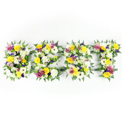 A refined, horizontal floral lettering arrangement spells BEST across a bright white backdrop, each letter meticulously built from a lavish mix of flowers and rich foliage. The image is shot straight-on with soft, consistent lighting that brings out the crisp whites and warm yellows at the heart of the design; large white chrysanthemum-like blooms and cream gerberas create a serene, textural base, while sunny yellow roses and gerbera daisies cast an uplifting, radiant tone through the composition. Smatterings of soft mauve and lavender lisianthus or similar small purple blooms sit quietly among the brighter tones, adding depth and a sense of calm, and bold magenta-pink spray roses or carnations give lively accents. Small clusters of pale green and white filler flowers are tucked between the larger heads to add delicacy and tactile variety. The letters are edged and softened with dark green fern fronds whose feathery leaves create a natural border and guide the eye along each character. A discreet dark-green or metal framework peeks through in narrow gaps - most notably along the E's horizontal arm and the T's bar - indicating the sturdy workmanship beneath the florals. The arrangement suggests a respectful memorial or a celebratory commendation, conveying warmth, esteem and fond remembrance. As a local florist in Clerkenwell I picture this placed with care near Leather Lane or delivered for a service at a nearby chapel, its fresh scent of roses and green foliage offering quiet consolation.