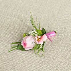 This Clerkenwell-inspired floral boutonniere, artfully composed on a pale, natural linen surface reminiscent of local artisan studios, is a true testament to thoughtful craftsmanship. The central blush-pink rose-fresh, tight, and gently spiralled-captures the gentle anticipation that often graces wedding mornings in nearby St James's Gardens. Embracing the rose is a ruffled, lighter pink blossom, likely an alstroemeria, its inner petals whispering of pale yellow and slender inky lines. Around them, delicate white sprays of baby's breath and vivid, textured green button mums are nestled, echoing the fresh vibrancy found in Clerkenwell's green spaces. Fern-like sprigs and dark, lustrous foliage create support and structure, some leaves folded with the care of an experienced hand, others fanning out in elegant arcs like the modern architecture nearby. The arrangement is tied neatly with a glossy fuchsia satin ribbon, its rich hue mirroring the festive spirit in the air during Clerkenwell weddings and gatherings. The neutral, coarsely woven backdrop provides a gentle contrast that enhances each floral detail and soft shadow. With every component-from the finely detailed petals to the tactile interplay of ribbon and leaf-this boutonniere carries the romance and intimacy of special occasions held within this vibrant London community, evoking memories that linger quietly, like the first scent of a summer morning in St John's Square.