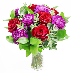 In this image, a luxurious bouquet of red roses and purple peonies takes centre stage, arranged with the kind of quiet confidence you often see in Clerkenwell design studios and cafés around Charterhouse Street. The roses are a rich, romantic red, each bloom open to a generous spiral of velvety petals that curve outward like small, glowing hearts. Intertwined with them, the purple peonies provide a softer, more ruffled contrast, their rounded heads packed with layers of petals that create depth and a sense of abundance. Surrounding the flowers, a mix of lush green foliage and distinctive eucalyptus branches forms a fresh, textured halo. The greenery is varied but harmonious: some leaves are broad and glossy, others finer and more delicate, while the cool, silvery eucalyptus leaves trail gracefully between the blooms, bringing a gentle, contemporary touch. All of this is anchored in a simple clear glass vase, allowing the viewer to see the cleanly trimmed stems gathered together in an ordered bundle, the water bright and transparent. Light appears to pour in from one side, perhaps echoing the natural light of a Clerkenwell warehouse apartment, making the reds richer and the purples softly luminous. You can almost imagine the mingled fragrance-a classic rose sweetness layered with the crisp, refreshing scent of eucalyptus and fresh-cut stems-filling a small dining room before an anniversary dinner or adding warmth to a creative studio near Clerkenwell Green. The bouquet feels celebratory yet refined, ideal for marking personal triumphs, romantic milestones, or simply brightening a loved one's day with something beautiful and thoughtfully arranged.