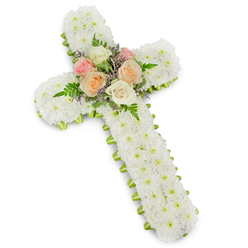 A traditional Christian cross made entirely of flowers fills the frame, set against a spotless white background that enhances every contour of the design. The main structure is built from tightly massed white button chrysanthemums, their petite blooms creating a thick, plush surface that feels almost like soft snow under the fingertips. No stems or gaps are visible, only an immaculate field of white petals that conveys innocence, serenity, and the quiet dignity often felt in Clerkenwell's older chapels and memorial spaces. Tracing the outline of the cross is a smooth lime green ribbon, wrapped neatly so that just a fine edge of colour shows around the borders, giving definition and a sense of careful craftsmanship. At the centre, where the beams cross, the mood changes slightly with a tender focal cluster of roses. These larger blossoms are fully open in harmonious pastel tones-delicate blush pink, gentle peach, and creamy white-arranged with airy green fern fronds that arch softly outward. Tiny accents of pale lavender or light purple filler flowers weave between the roses, adding a hint of contrast and drawing the eye to the heart of the tribute. The lighting is even and calm, emphasising texture rather than drama, making it easy to imagine this cross resting beside a casket or standing by a memorial photograph during a service. Created with the care of an experienced local florist, it serves as a heartfelt funeral flower tribute, offering comfort and a visual expression of sympathy to families across Clerkenwell and the surrounding central London neighbourhoods.