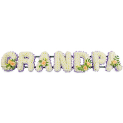 The word GRANDPA stretches in a steady horizontal line, each capital letter formed entirely from fresh flowers, like a soft white banner of remembrance ready to rest beside a coffin or at the front of a service in Clerkenwell. Every letter is completely covered in small, pristine white chrysanthemums, their layered petals creating a dense, pillowy texture that feels both gentle and reassuring, much like the presence of a beloved grandparent. Along the edge of each letter, a refined border of light lavender blooms traces the outline, a cool purple ribbon that softly separates the white flowers from the clean background and draws the eye along the sequence of G, R, A, N, D, P, A. The colour harmony of white and lilac suggests calm reflection, similar to the quiet corners found along Clerkenwell Green or near the old stone buildings off Farringdon Road.   

In carefully chosen places, accents of peach roses introduce warmth and personal character. On the strong curve of the G and the upright of the D, modest clusters of peach roses are tucked into lush, dark green foliage, with a few slender white lily buds adding height and contrast. The first and final A each bear a single peach rose, like a whispered farewell at the beginning and end of the name. These soft, sunset tones speak of affection, gratitude, and cherished family stories. A narrow, dark support bar runs behind the lower half of the letters, giving subtle structure without disturbing the visual softness. The overall effect is one of dignity and tenderness, a bespoke floral tribute suitable for funeral and memorial services across Clerkenwell, Farringdon, and the surrounding EC1 community.