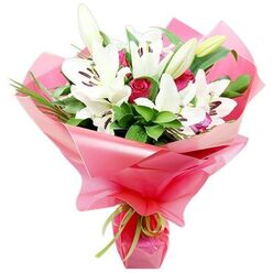 A richly detailed bouquet of pristine white lilies and deep red roses is shown in close focus against a seamless white background, giving the flowers a stage-like presence. At the heart of the design, several Oriental lilies open into wide, star-shaped trumpets, their pure white petals curving back slightly to frame clusters of dark, cocoa-brown anthers perched on slender filaments. Some lilies are fully open, while others remain as elongated, green-tipped buds, suggesting an arrangement that will keep evolving over several days. Threaded between the lilies are multiple red roses in bud and early bloom, their tightly packed petals forming spirals of velvety colour that deepen towards the centre like pools of wine. Encircling the blooms, a generous mass of rich green foliage, from broader polished leaves to fine, blade-like greenery, creates an impression of abundance and structure, guiding the eye upwards through the bouquet. The stems are enveloped in bright, glossy pink cellophane or floral wrap, softly crinkled and folded to form voluminous ruffles that catch the light and give a sense of movement, as if the bouquet were wrapped moments ago in a busy Clerkenwell flower studio near St John Street. At the base, a slim lime green ribbon is tied neatly, its satin surface glinting subtly and providing a refreshing note that links the wrapping to the foliage. The whole arrangement feels joyful, romantic, and polished-an ideal floral gift for birthdays, Mother's Day, or a spontaneous "thinking of you" delivered to homes and offices around Farringdon, capturing both tenderness and a touch of London sophistication.