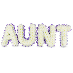 Here, the name AUNT is crafted in bold, capital letters using hundreds of small, snow-white spray chrysanthemums-each bloom tightly packed to form plush, textural surfaces that soften the strong verticals and sweeping curves of the lettering. Tiny pale yellow centres glimmer within the white petals like the smallest of heartbeats, a gentle counterpoint to the overall purity of the design. A rich purple satin ribbon hugs the perimeter of every letter, its pleated edge forming a scalloped frame that adds a thoughtful pop of colour and a tactile contrast to the soft chrysanthemums. From a florist's perspective, the construction reads as both sturdy and tender: the frames are solid enough to stand clearly during a funeral service yet cushioned by the flowers so the tribute feels like a careful embrace. Soft studio light highlights the satin sheen of the ribbon and creates delicate grey shadows beneath each letter, reinforcing their three-dimensional presence against the white background. There is a quiet, green-fresh scent to the arrangement and a faint texture under the fingertips where the petals overlap. Locally made in Clerkenwell and commonly requested for services near Spa Fields and St James's Church, this style communicates dignified remembrance with an undercurrent of affection. Clerkenwell Flowers prepares these tributes with attention to longevity and respectful presentation, arranging and delivering them thoughtfully to ensure they arrive fresh and complete for memorial gatherings and wake services across the neighbourhood.