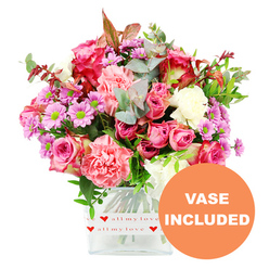 Against a bright, uncluttered white background, a vibrant mixed bouquet radiates warmth and care, like a love note arranged in flowers for someone living near Clerkenwell's historic squares and cobbled lanes. The composition is grounded in a clear, square glass vase, its lower section wrapped in a white band decorated with small red hearts and the tender phrase "all my love," instantly signalling that this is meant as a heartfelt gift rather than a casual bunch. Emerging from the vase, the flowers gather in a rounded, slightly domed shape, with generous pink roses taking centre stage. Some roses are a rich, almost raspberry fuchsia, while others soften into pastel pink, their layered petals unfolding with a plush, velvety texture. Interwoven among them, peachy and coral-pink carnations with finely ruffled edges create a sense of fullness and movement, as though the bouquet is gently breathing. Throughout the design, smaller daisy-like chrysanthemums in lavender and purple, each with a bright green eye, punctuate the arrangement with playful, zesty touches of colour. Creamy white carnations and daisy-style blooms soften the bolder tones, giving the whole bouquet an airy, uplifting feel. Lush greenery frames the blossoms: rounded eucalyptus leaves in cool blue-green, deeper glossy foliage, and a few reddish-brown leaves that hint at late-summer evenings along St John Street. The stems are visible through the crystal-clear glass, neatly aligned and trimmed to sit securely in the water. An orange circular badge appears in the bottom right corner of the image, with the words "VASE INCLUDED" in crisp white capitals, clearly indicating this is a complete, ready-to-enjoy floral gift, ideal for sending love, thanks, or congratulations anywhere in and around Clerkenwell.