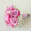 On a gentle linen cloth that echoes Clerkenwell's creative calm, a chic, hand-crafted bouquet takes centre stage. Five lush roses unfold in symphony, their petals shifting from soft lavender hearts to bold magenta edges, the colours alive with vibrancy. Wisps of dainty white gypsophila nestle between the rose blooms, lending a delicate, almost whisper-light texture that softens the whole composition. The handle of the bouquet is enveloped in plush, deep purple ribbon, finished with elegant spirals of pearl beads-a flourish that might be spotted in the design shops of Clerkenwell, known for their attention to artistry and detail. Bare stem ends peek beneath the ribbon, celebrating the natural beauty beneath the crafted surface. Soft daylight caresses the bouquet, revealing a fresh, dew-kissed quality and inviting thoughts of new beginnings. This arrangement conveys love, sophistication, and the quiet excitement of a wedding, whether destined for the Old Sessions House or a Clerkenwell loft celebration. Crafted by obsessive local hands, it offers a floral keepsake that radiates both joy and meaning, perfectly suited to any romantic or ceremonial milestone in EC1.