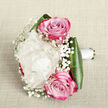 Seen from a slightly raised perspective, this graceful bouquet lies against a pale, linen-like fabric in soft beige tones, the neutral background allowing every detail of the flowers to stand out. At the centre, a single creamy white peony unfolds in layer upon layer of plush petals, round and cloud-like, its fullness giving the arrangement a sense of gentle opulence. Nestled close to it are two pink roses, one poised just above and the other beneath the peony, each with a tight spiral core that gradually releases into velvety petals edged in richer magenta. Their colour shift from soft pink to deeper fuchsia adds a sophisticated, romantic tension, neither too bold nor too pale. Dancing between the main blooms are airy sprigs of white baby's breath, their clusters of tiny blossoms creating a misty, almost lace-like effect that lightens the whole design. Dark, glossy leaves form a protective collar at the base, curving smoothly around the stems and framing the blooms with deep green structure. The stems themselves are wrapped in a clean white satin ribbon, neatly tied to suggest a bouquet made to be held down the aisle, perhaps by a bride walking from Clerkenwell Green towards a nearby reception. The lighting is gentle, flattering the textures of petal and leaf, and the bouquet carries an overall feeling of romance, care, and celebration, perfectly suited to wedding features, local bridal inspiration, or special occasion gift ideas in the Clerkenwell area.