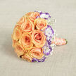 Captured from a slightly elevated viewpoint on a warm beige linen backdrop, this round bridal bouquet feels like a soft sigh of affection. The composition centers on abundant peach and soft orange roses, their petals layered in gentle spirals that catch a diffuse, natural light and glow with a warm inner radiance. Interspersed among the roses are white lisianthus blooms with ruffled edges tipped in deep violet, their cool-toned margins sharpening the arrangement's palette and introducing an artful, contemporary contrast. Tiny clusters of white baby's breath drift between the larger flowers, whispering of innocence and adding a light, feathery texture that offsets the roses' sumptuous density. The stems are neatly wrapped in a pale peach-coral satin ribbon, which extends from the lower right and is encircled by a string of cream pearls, lending a refined, tactile finish that invites touch. The bouquet is styled to feel both classic and modern-an emblem of partnership and celebration, faintly scented with fresh roses and made to be held close at the altar or during a small, sunlit ceremony in and around Clerkenwell and nearby Exmouth Market. The photograph emphasizes craftsmanship, colour harmony, and a mood of hopeful intimacy, suitable for weddings, vow renewals, or anniversaries where thoughtful detail matters.