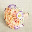 An elegantly hand-tied bridesmaid bouquet rests atop an oatmeal-toned linen cloth, glowing in the natural light streaming through a Clerkenwell window. At its heart, plush peach roses with creamy, softly blushing petals mingle with pristine white Lisianthus, their ruffled edges boldly painted in violet-a striking, contemporary twist. Delicate Baby's Breath provides featherweight balance and a whisper of old-world romance, its tiny blooms interspersed like clusters of small clouds. The bouquet's rounded shape is artfully compact, its stems neatly finished with a peach-satin ribbon and a discreet line of luminous pearl beads, the hallmark of attentive craftsmanship found along the creative streets of Clerkenwell. The palette-warm, refined, and inviting-makes this arrangement ideal for weddings across the area or as an inspired centrepiece at a reception in the heart of Farringdon. Lush, fragrant, and alive with thoughtful detail, this bouquet captures the spirit of a celebratory day amidst Clerkenwell's artistic community.