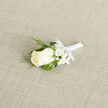 Resting diagonally on a warm, light-beige woven fabric, this boutonniere centres on a singular, immaculate ivory rosebud whose velvety layers gather inward like a quiet vow. Around it, tiny sprays of snow-white gypsophila create a delicate halo, their cloud-like clusters softening the composition and allowing the rose to remain the undisputed focus. Counterpointing the blooms, slender, feathery sprigs of dark-green foliage-suggestive of cedar or evergreen-arc gracefully, adding a cool, slightly resinous texture, while more substantial deep-green leaves provide a solid, supportive backdrop that grounds the design. The stems are bound with a smooth white satin ribbon, finished in a small, precise bow that reads as modest ceremony rather than flourish; the ribbon's satin sheen catches the light and links each botanical element. The subtle woven textile below lends a natural, tactile warmth, making the whites and greens appear fresher and more distinct. One can imagine this boutonniere available from Clerkenwell Flowers, the kind of carefully finished piece we make for couples planning a small wedding near Clerkenwell Green or an intimate ceremony by Spa Fields; the piece speaks to local taste for quiet, considered detail. There is a faint, uplifting scent suggested by the rose and greenery, a clean, gentle presence rather than something overpowering. Overall the arrangement balances tradition and restraint-an elegant, wearable emblem of new beginnings to be pinned close to the heart on a day that values simplicity and care.
