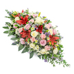 A dignified, double-ended funeral spray is shown against a pure white backdrop, its form and colours carefully arranged to convey respect and gentle comfort. The composition is elongated and symmetrical, designed to sit gracefully atop a coffin, with the fullness of the flowers concentrated at the centre and softly tapering towards each end. Deep red Oriental lilies form the emotional centre of the piece, their large, star-shaped blooms opening wide, each petal richly coloured and slightly curved, adding drama without overpowering the overall serenity. Surrounding them, clusters of cream, ivory, and blush-toned roses unfold in various stages, from tight buds to open rosettes, suggesting affection, remembrance, and quiet devotion. Light pink spray carnations add a cloud-like softness, their frilled petals catching the light, while smaller white chrysanthemum and daisy-like flowers bring a touch of brightness and intricacy. Scattered among these are accents of cool blue-purple, including slender spires of filler flowers and thistle-like blooms that introduce texture and a subtle modern edge. The entire design rests in a cradle of deep green foliage, with shiny, broad leaves layered beneath lighter, trailing greenery that spills gently over the imaginary edges of a casket, creating a natural frame. It feels like a piece created by a local Clerkenwell florist who understands the area's blend of tradition and contemporary life, suitable for delivery to nearby funeral homes or chapels. The spray speaks softly of sympathy and everlasting love, offering a refined and comforting tribute at a time of loss.
