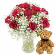 A serene, all-white background provides a clean stage for a romantic floral and plush gift pairing that feels perfectly suited to a Clerkenwell apartment overlooking Exmouth Market. On the left, a generous bouquet of about one dozen deep red roses stands tall in a clear glass vase. The roses are rich and velvety, their petals layered in tight, luxurious whorls that gradually unfurl into full, rounded blooms. Each flower shows subtle variations in crimson, from darker, almost burgundy shadows at the centre to slightly brighter red edges where the light touches. Nestled among the roses are airy sprays of white baby's breath, their tiny blossoms forming a fine, cloud-like network that softens the intense red and gives the arrangement a gentle, romantic glow. The stems, visible through the glass, are trimmed neatly and immersed in fresh water, hinting at careful preparation in a nearby Clerkenwell flower shop. To the right of the vase, a medium-sized teddy bear sits poised and welcoming. Its light brown plush fur appears soft and slightly textured, inviting the touch, while round, dark button eyes, a delicate stitched nose, and a small, curved smile lend it a reassuring, affectionate character. A narrow dark brown ribbon is tied in a neat bow around its neck, adding a touch of understated elegance. The composition is calm yet emotionally expressive, evoking the feeling of receiving a same-day delivery to a creative studio along Farringdon Road-a heartfelt surprise for anniversaries, Valentine's Day, birthdays, or any moment when words are not quite enough to convey love and appreciation.