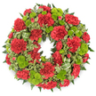 Set against a smooth white background, a full, circular wreath of red and green flowers appears almost to float, its colours vivid and carefully balanced in a classic funeral tribute. The main impression is of deep, velvety red, created by a ring of tightly clustered carnations whose ruffled petals layer over one another to form rich, soft mounds of colour. Threaded throughout these crimson blooms are bright lime green button chrysanthemums, their tidy, spherical shapes providing a crisp contrast, as if beads of fresh spring green had been scattered evenly across the wreath. The entire arrangement is framed and underpinned by lush green foliage: dark, feathery fern fronds add a delicate fringe, while variegated leaves with pale, creamy edges and darker centres introduce gentle movement and pattern. A subtle striped ribbon in coordinating green tones is woven near the base of the wreath, its simple loops echoing the circular form and lending an understated elegance. The lighting is bright and even, typical of a professional studio in Clerkenwell, allowing every petal, leaf, and shadow to be seen clearly and highlighting the craftsmanship involved. The design sits comfortably between traditional and modern, making it an appropriate choice for funeral services, church ceremonies, or cremations in and around Clerkenwell, from historic churches near Smithfield to quieter chapels off Clerkenwell Road. Emotionally, the red suggests deep love and respect, while the lime green hints at renewal and lasting memory, offering comfort to families and friends gathering to say goodbye.