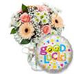 A bright, hopeful 'Good Luck' gift set captured against a clean white studio backdrop: on the left a generous, homey bouquet sits in a clear glass vase tied at the neck with rustic twine, the kind of simple detail you notice when you hold stems in your hand. The arrangement is built from soft peachy-orange Gerbera daisies with their dark, chocolatey centres, tightly furled light-pink roses that read as gentle and reassuring, clusters of tiny white baby's breath (Gypsophila) that spill like lace, and small white-and-lime-green chrysanthemum florets that add a crisp pop of freshness. Deep green foliage threads through the composition, giving shadow and depth to the pastel faces of the flowers; you can imagine the subtle rose perfume and the dry, clean scent of the gypsophila when you lean in. To the right and slightly overlapping the lower part of the vase is a round metallic foil balloon with a shimmering silver-white surface, scattered with colorful stars, hearts and confetti-like marks in blue, pink, yellow and green. Across the balloon the phrase Good Luck! appears in playful multi-coloured letters - the two 'o's in Good are cheerful yellow smiley faces, one winking and one sticking its tongue out - the typography feels buoyant and informal. A small brand mark sits low on the balloon's curve, adding a crisp commercial finish. The whole composition radiates encouragement and quiet celebration: it reads as a tactile, scented bouquet paired with a joyful balloon, suitable for exam send-offs, interview wishes, graduations or a caring farewell locally delivered across Clerkenwell and nearby streets like Exmouth Market or Leather Lane.