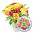 A vibrant, thoughtfully composed Get Well Soon gift arrangement captured against a clean white backdrop, described as if I were handing it to a neighbour from Spa Fields Park. On the left, a lush bouquet spills from a clear glass vase, the water and a tangle of stems visible through the glass. The eye is drawn to several large, soft orange-to-deep yellow roses, their velvet petals unfurling in gentle spirals and giving off a faint, citrus-tinged scent that feels like a small lift of spirits. Intermingled with the roses are sunny yellow gerbera daisies, their broad faces bright and open like miniature suns, and deep burgundy or maroon carnations that add ruffled texture and a grounding contrast. Scattered throughout are delicate sprays of white alstroemeria, their fine petals and subtle markings lending an airy, graceful balance to the denser blooms. Glossy, verdant foliage-varying leaf shapes and sizes-cradles each stem, adding freshness and a natural silhouette to the composition. To the lower right the bouquet is playfully punctuated by a round, metallic silver Mylar balloon: its mirrored surface catches soft daylight and frames a cheerful cluster of cartoon-style balloons in blue, purple, green, pink and yellow, some patterned with stripes, polka dots and checkerboards. Bold yellow-and-blue letters with a gentle shadow proclaim Get Well Soon across the centre, and tiny starburst accents around the white border amplify the upbeat message; a small KALEIDOSCOPE logo sits at the balloon's bottom edge. The overall feeling is warm, hopeful and expertly balanced-an uplifting gift suited to bedside cheer or delivery to friends and family near Clerkenwell's local streets and markets.