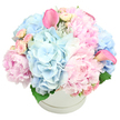 A generously filled white hatbox sits against a clean white background, overflowing with pastel blooms that create a soft, romantic impression. At first glance, the eye is drawn to large, rounded clusters of light blue hydrangeas, their many delicate petals forming a cushiony base that looks as soft as a cloud above Clerkenwell's cobbled lanes. Blush and baby pink hydrangeas mingle with the blue, adding depth and a gentle transition of colour, as if the arrangement is capturing early morning light. Nestled between these rounded forms are lush pink peonies, some fully opened into frilly, layered cups, others still partially closed, suggesting the quiet promise of petals yet to unfold. Smaller pink spray roses and neat rosebuds peek out from the spaces between larger flowers, introducing fine texture and intimate detail, like little secrets hidden within a garden. Two vivid pink calla lilies rise elegantly from the composition, one leaning to the left and one to the right, their sleek trumpet shapes and smooth surfaces offering a contemporary note that feels at home in a modern Clerkenwell apartment. A handful of rich green leaves can just be seen at the base, offering contrast and structure to the pastel tones above. The flowers are arranged in a dense, rounded dome that gently spills over the rim of the box, suggesting generosity and care. This arrangement would suit a new baby celebration near Farringdon, a springtime birthday dinner by St John's Square, or a comforting, elegant gesture of sympathy delivered to a friend's home. The overall effect is one of soft luxury, calm joy, and thoughtful craftsmanship from a skilled local florist.