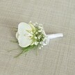 A single white orchid boutonniere rests gently on a softly textured light beige fabric, the weave of the cloth reminiscent of natural linen you might find in a Clerkenwell design studio. At the heart of the arrangement sits a pristine Phalaenopsis orchid bloom, its broad, velvety petals a clear, luminous white that glows against the neutral background. The orchid's throat reveals a delicate touch of pale yellow and the faintest hint of cream, suggesting freshness and quiet warmth, as though it has just been prepared in a local flower shop before a ceremony near Exmouth Market. Surrounding the central orchid are airy clusters of tiny white baby's breath, their cloud-like blossoms adding a misty softness and a sense of lightness to the design. Slender strands of feathery green foliage, similar to asparagus or maidenhair fern, peep out from beneath the flowers, bringing a touch of woodland freshness and gentle movement. The stems are neatly and firmly wrapped in smooth white satin ribbon, the fabric pulled tight and finished with a small, understated bow positioned close to the base, signalling that the piece is ready to be pinned to a lapel. The lighting is calm and even, with no harsh shadows, creating a serene, intimate mood that feels suited to a wedding morning in Clerkenwell, perhaps in a historic town hall or a stylish converted warehouse. The overall impression is of refined, minimalist elegance: a classic orchid boutonniere that speaks of purity, commitment, and thoughtful craftsmanship, perfect for a groom, groomsman, or formal guest who values subtle, contemporary style.