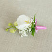 This image shows an elegant boutonniere lying on a softly woven, natural linen surface in a warm oatmeal shade, the understated background chosen to highlight the delicate craft of the flowers. At the centre is a flawless white Phalaenopsis orchid, its wide, curved petals smooth and luminous, almost like fine china set under calm indoor light. The orchid's throat holds a gentle flush of yellow-orange with just a hint of pink, lending warmth and depth to the otherwise pure white bloom. Gathered close around it are airy sprigs of white Gypsophila, or baby's breath, forming a soft cloud that frames the orchid and adds a romantic, almost ethereal texture. A few slim, glossy green leaves are tucked among the blooms, introducing a fresh, botanical line that brings the whole piece to life. To the left, a slender stem stretches out, carrying three rounded, pale green orchid buds that have not yet opened, suggesting quiet growth and the anticipation of the celebration ahead-be it a wedding at a Clerkenwell registry office or a formal event near Farringdon. The lower part of the buttonhole is neatly wrapped in a bright pink satin ribbon, its surface shining subtly and tied into a compact, decorative bow with short, tidy tails. The light catches the ribbon just enough to contrast with the soft matte texture of the linen beneath it. The overall composition is balanced, calm, and contemporary, a refined floral accent crafted by a skilled florist and perfectly suited to add a touch of understated luxury to any lapel in and around Clerkenwell.