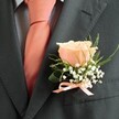 There is a timeless grace in this classic buttonhole-so often chosen by couples celebrating love in Clerkenwell's character-filled venues near Exmouth Market. At the heart rests a singular rose, its petals softly blushing in shades of peach that light up against the structured charcoal jacket, evocative of refined celebrations at St John's Square. Around the rose, breath-light clouds of baby's breath add texture and airiness, catching the natural light like dew on early spring mornings in Finsbury. Sprigs of vibrant greenery-perhaps ruscus or fern-arc gently to complete the verdant, uplifting mood. Tied at the base, a sleek bow in peach satin mirrors the polished necktie, uniting every element in a harmonious flourish. There's a gentle fragrance, hinting at garden freshness and tender moments, carried lightly on the air. As a local florist, one understands that such buttonholes are more than accessories; they're tokens of unity and hope, crafted with sensitivity and care to rest proudly at the heart of milestones-be it a wedding in Clerkenwell, a formal supper near Charterhouse Square, or a celebration just steps away from the storied lanes of London's creative heart.