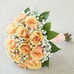 This exquisite hand-tied bouquet, a signature creation inspired by the thoughtful atmosphere of Clerkenwell, radiates delicate romance and timeless poise. At its center, a rich cluster of fully opened peach and apricot roses showcases petals that softly transition from gentle cream to glowing, sunlit orange. Interlaced with the roses are wispy bands of pure white baby's breath, each tiny flower scattering like lace along the edges, giving the bouquet a light, whimsical aura reminiscent of a celebratory afternoon on Clerkenwell Green. Deep green leaves-lush and glossy-surround the bouquet, providing contrast and depth, much like the verdant gardens tucked around this creative district. The stems are elegantly gathered with a wide, peach-hued ribbon that wraps smoothly in the hand, its surface detailed with a grid of petite pearls, echoing the classic touches found at stylish local weddings. Resting diagonally on a woven cream-coloured fabric, every bloom and leaf is illuminated by gentle daylight, capturing the texture and nuance of the composition. The soft scent of fresh roses and crisp greenery rises from the bouquet-a gentle breath of nature, evoking feelings of hope, love, and anticipation. Perfect for a wedding ceremony, a vow renewal, or as a thoughtful gift, this bouquet reflects Clerkenwell's charm, artistry, and sense of occasion, making unforgettable moments even more special.