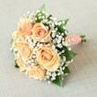 A timeless hand-tied bouquet, brimming with soft peach and apricot-hued roses, is arranged with artful precision and placed atop a gently textured linen surface-its character reminiscent of Clerkenwell's eclectic blend of history and modern artistry. Each of the seven to nine roses in the bouquet appears at the height of bloom, their centres tightly curled, petals gradually unfurling into ruffled edges that catch the light like the first blush of dawn on Clerkenwell Green. Among the focal blooms, fine white clouds of baby's breath (Gypsophila) add a touch of airy grace, offsetting the roses' inviting warmth with their ethereal beauty. Small flashes of deep emerald green rose leaves contribute depth and a subtle fragrance, suggestive of a fresh garden cut just off St. John Street. The stems, gathered and finished with a beautifully wrapped coral-peach ribbon spiralled with tiny white faux pearls, offer a tactile, almost vintage approach-evoking classic wedding styles celebrated in the neighbourhood's chic venues. The harmonious rounded shape of the bouquet rests gently, bathed in soft, natural light that reveals every detail-from the intricate layering of petals to the elegant pearl accents. Created for a memorable Clerkenwell occasion, this bouquet would suit weddings, anniversaries, or any heartfelt event, encapsulating the area's spirit of romance, artistry, and enduring connection.