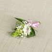 A delicately handcrafted floral buttonhole rests on a softly textured, light beige linen-style cloth, the neutral background allowing every detail of the design to stand out as if laid on a table in a quiet Clerkenwell townhouse. At the heart of the arrangement sits a single white alstroemeria bloom, its open petals broad and slightly ruffled, brushed with fine reddish-brown speckles that gather toward the throat of the flower like gentle strokes of watercolour. The alstroemeria's stamens are visible, lending a sense of freshness and immediacy, as though the flower has just been prepared for a wedding morning near Exmouth Market. To one side rises a compact, conical cluster of vivid lime-green buds, reminiscent of Ornithogalum, each tiny segment packed closely together to create a sculptural, almost architectural contrast against the softness of the lily. Around these focal elements, airy sprays of white baby's breath drift like miniature clouds, filling the negative space with a light, almost misty texture. Supporting everything is a base of lush greenery: strong, dark green, spear-shaped leaves form a solid backdrop, while slender, grass-like strands weave in and out, adding subtle movement and a sense of garden spontaneity you might find strolling through local pockets of green near Clerkenwell Green. At the right, a narrow, glossy satin ribbon in a bright, cheerful pink is tied into a small, neat bow, cinching the stems with a celebratory flourish that hints at romance and joyful gatherings. The lighting is even and soft, with no harsh shadows, gently revealing the interplay between the velvety petals, glossy foliage, and smooth ribbon. The overall mood is one of quiet elegance and heartfelt craftsmanship, a compact floral accessory perfectly suited to a lapel or wrist for weddings, proms, or intimate celebrations across Clerkenwell.