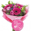 A bright and tender maternity gift arrangement appears against a clean white backdrop, consisting of a hand-crafted pink bouquet and a cheerful balloon that would look perfectly at home in a Clerkenwell apartment or office. The flowers are arranged in a rounded, generous cluster, dominated by fuchsia gerbera daisies whose dark centres contrast sharply with their luminous rings of petals. These gerberas create an immediate sense of joy, like little suns peeking out from the bouquet. Between them, soft pink roses add a romantic, gentle note. Some roses are still somewhat closed, with their outer petals wrapped protectively around the inner layers, while others open further, revealing nuanced spirals and a velvety texture that suggests both delicacy and strength. Tiny purple filler flowers are scattered throughout, creating soft, cloud-like bursts of colour that weave in and out of the pink blooms. A collar of fresh greenery surrounds the flowers, the leaves ranging from slim and elongated to wider and slightly glossy, contributing to a rich, multi-dimensional texture. The stems are bundled and wrapped in layered sheets of pink tissue paper, from pale pastel to bold magenta, folded to create a ruffled, almost tutu-like skirt around the base. Over this sits a clear cellophane layer that reflects light and underscores the bouquet's ready-to-gift styling, reminiscent of arrangements prepared by Clerkenwell Flowers for same-day delivery. Resting at the bottom front of the bouquet, a round foil balloon adds a playful, personal touch. It is a vibrant fuchsia pink scattered with crisp white polka dots, finished with a gently scalloped edge. The words Mum to Be! sweep across the centre in flowing white script, with a white heart surrounding a smaller pink heart positioned between the words, symbolising the new life held within. The overall impression is one of heartfelt celebration and anticipation, perfect for marking pregnancy milestones around Clerkenwell and Farringdon.