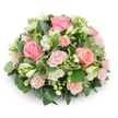 A soft, dome-shaped memorial spray composed of tightly clustered pale pink roses and crisp white freesias rests against a pure white backdrop, the composition exuding quiet comfort and refined simplicity. The dominant roses range from fully unfurled, velvety blooms in deeper blush and salmon tones to smaller, delicate spray roses in palest pink, their layered petals forming gentle spirals that invite a touch. Scattered between the roses are upright stems of white freesia: some bells open to reveal tiny yellow stamens and a light, sweet fragrance, others still elegant buds that promise continued opening. The arrangement sits densely packed with no visible stems, creating a cushion-like silhouette punctuated by glossy dark-green leaves-likely salal or ruscus-that provide a solid, verdant foundation. Variegated foliage with cream-edged margins (suggestive of pittosporum) threads through the bouquet, catching the light and brightening the palette without intruding on the tenderness of the pinks and whites. Natural daylight from the left softens the textures, highlighting the velvety rose petals and the freesia's translucent tips while casting a gentle shadow that enhances the rounded shape. The overall effect is one of considered craftsmanship: compact, balanced, and sympathetic in mood. I picture this piece on a low table at Clerkenwell Green or beside a lit memorial candle during a service at a nearby chapel, its understated palette offering solace and calm. The scent is quietly floral rather than overpowering, and the freshness of the blooms suggests careful selection and immediate preparation, an arrangement that communicates tenderness, remembrance, and enduring care.