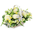 A light-toned wicker funeral basket with a gracefully curved handle is shown against a spotless white background, filled to the brim with a harmonious blend of soft, pastel flowers and fresh greenery. The arrangement is low, rounded and carefully balanced, suggesting both fullness and gentle restraint. At its centre, several large creamy white roses bloom in perfect symmetry, their velvety petals unfolding in layered spirals that radiate calm and purity. Threaded among them are distinctive pale lavender clematis blooms, star-shaped with fine pointed petals and vivid yellow-green centres, lending a touch of individuality and quiet beauty without breaking the tranquil mood. Around the focal flowers, clusters of white and pale yellow freesia-like blossoms curve naturally, some stems topped with tight buds, others with delicate, bell-shaped flowers that add fragrance and a sense of new beginnings. Additional white ruffled blooms, likely lisianthus or similar, deepen the lush texture and make the basket feel abundantly filled. A generous collar of dark, glossy leaves and lighter green shoots surrounds the flowers, providing contrast and framing the pastel tones in a way that feels both fresh and elegant. The overall impression is of a thoughtfully crafted sympathy arrangement, the kind that might be delivered to a family home off Rosebery Avenue or placed quietly in a chapel near Clerkenwell Green. It conveys respect, comfort and sincere condolences, offering a serene focal point at a time when words may be hard to find.