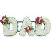 A reverent three-dimensional tribute spells out the word DAD in bold, capital letters, each letter fashioned from a dense carpet of pristine white chrysanthemums that give the surface a cloud-like, cushiony texture. The white blooms sit against a pure white backdrop so the sculpted shapes read cleanly; from a short distance the texture softens into a luminous, peaceful plane. Each letter is neatly edged with an emerald-green, pleated ribbon that traces the outer and inner contours, the cool green tone lifting the white into crisp definition and adding a dignified, almost military neatness. Small clusters of deep magenta roses, at varying stages from tight bud to half-open bloom, punctuate the letters: one cluster on the upper left curve of the first D, another tucked into the central V of the A, and a final grouping on the upper right of the last D. These rose clusters are brightened with delicate white freesia-like blossoms and glossy, dark green foliage, creating contrast in colour, sheen and scent-the roses' warm, honeyed perfume mingling subtly with the freesia's citrus sweetness. A discreet dark green support bar runs horizontally behind the letters, hinting at a self-standing memorial display suitable for a funeral, wake or graveside. The overall effect is quietly personal: traditional and respectful, with a touch of warmth from the magenta accents. As a local florist working from Clerkenwell and serving nearby Farringdon and Exmouth Market, I describe this piece as a bespoke sympathy lettering that reads as love, memory and gentle farewell.