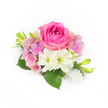A compact, elegantly arranged corsage set against a pristine white background, beginning with a plush bubblegum-fuchsia rose at its centre whose young petals coil inward before unfurling into a velvety bloom. Surrounding the central rose, clusters of pale pink and lavender hydrangea florets form a soft, cloud-like cushion that gives the piece gentle volume and a romantic air. Interspersed beneath and beside these blooms are two creamy white, trumpet-shaped flowers with faintly green throats-small amaryllis or lily-like blossoms whose satin petals catch the light and lend a feeling of purity. Glossy deep-green leaves spread beneath the composition, their broad texture grounding the arrangement and offering a cool contrast to the warm pinks. Slim, vibrant green buds edged with a hint of yellow reach upward, suggesting movement and the promise of more blooms to come. At the lower right a short cascade of luminous white pearls, varying slightly in size, adds an understated, heirloom sparkle, like a piece of bridal jewellery tucked into the bouquet. The overall impression is fresh, tactile, and quietly celebratory: petals that look cool to the touch, a faint garden fragrance imagined in soft daylight, and a refined silhouette ideal for weddings, proms, or anniversary corsages. As a local touch, this style suits brides and guests preparing for intimate ceremonies around Clerkenwell Green or quick pick-ups from nearby Exmouth Market, where florists often craft enduring, hand-finished pieces for special neighbourhood occasions.